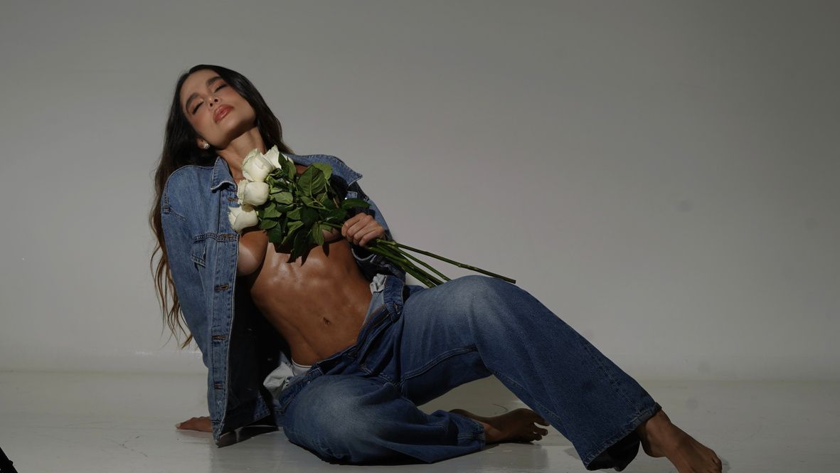 Tatiana Gaviria sentada con chaqueta de jean y rosas blancas en estudio