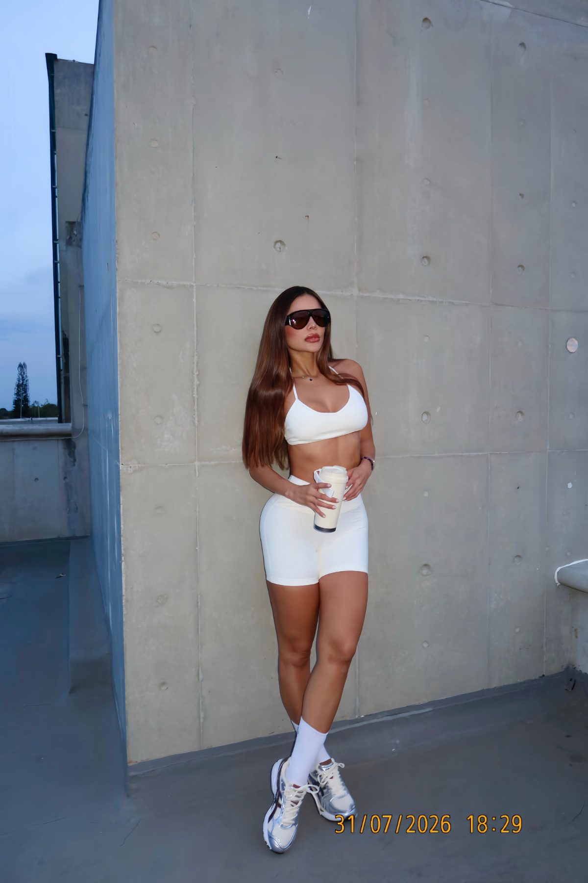 Tatiana Gaviria en conjunto deportivo blanco con gafas de sol, junto a un muro de concreto